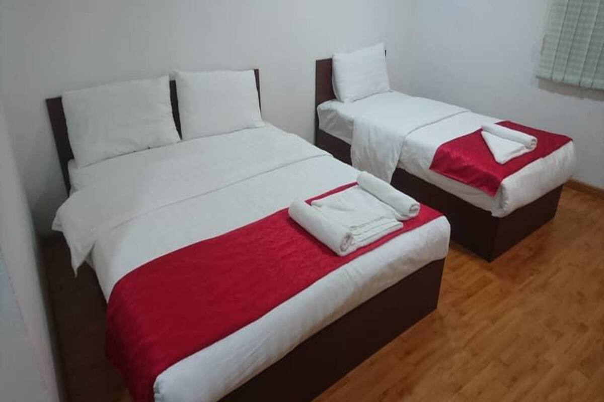 Dos camas individuales con ropa de cama blanca y detalles rojos, cabeceros de madera y piso de madera.