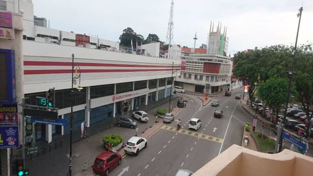 A street view with a bank, a red car, and a white car driving on the road.