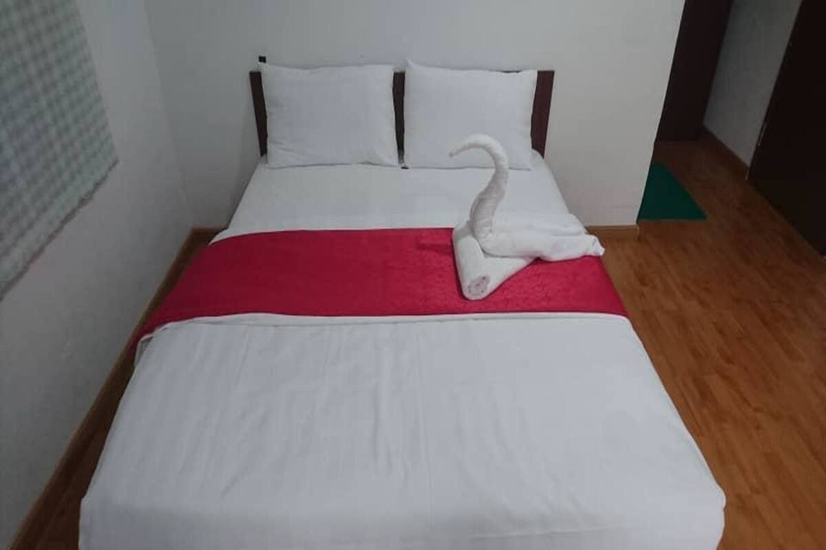 Una cama bien hecha con una manta roja y una toalla blanca en forma de cisne sobre ella.
