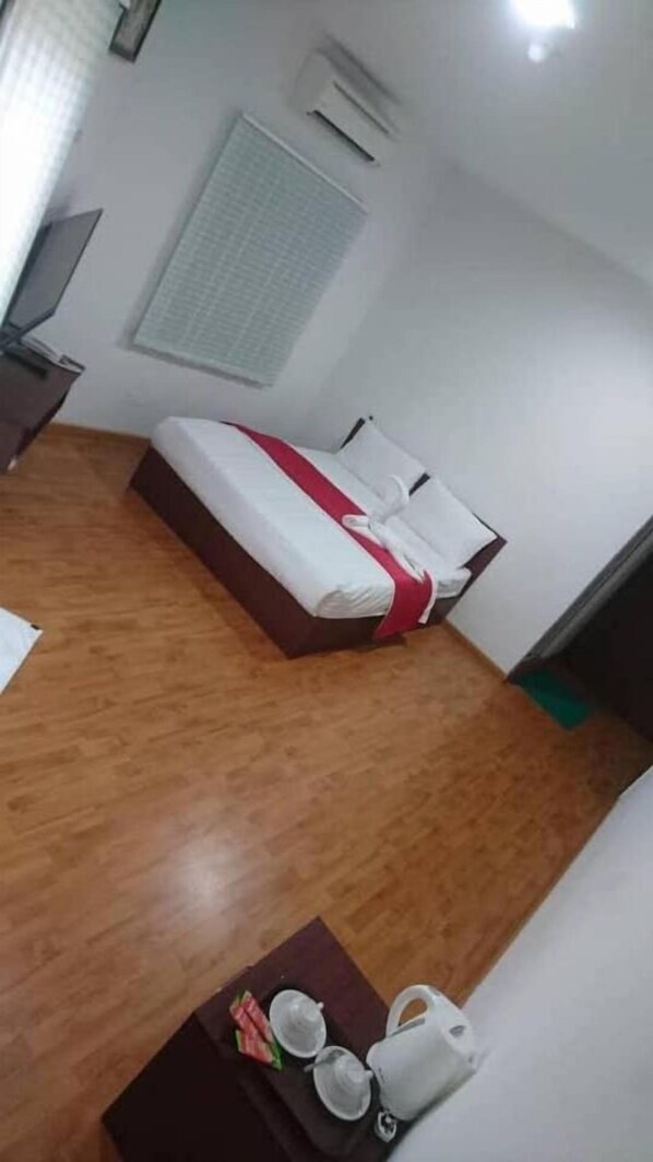 Une chambre d’hôtel avec un plancher en bois, un lit avec une literie blanche et rouge, une petite table sur laquelle se trouve un plateau avec du thé et des tasses, et un téléviseur posé sur un meuble.