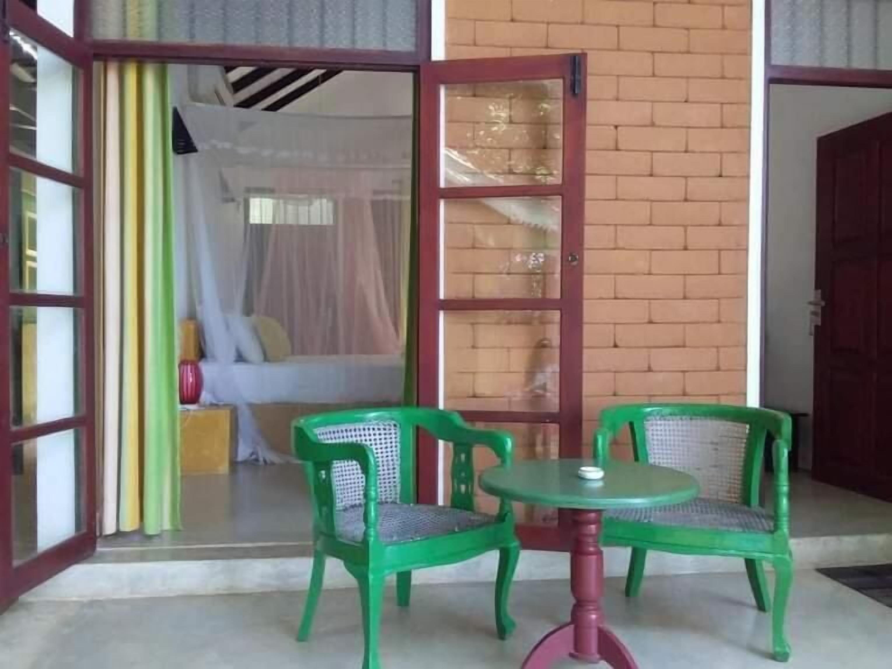 A room with a bed, a green chair, a table, and a glass door leading to a balcony.