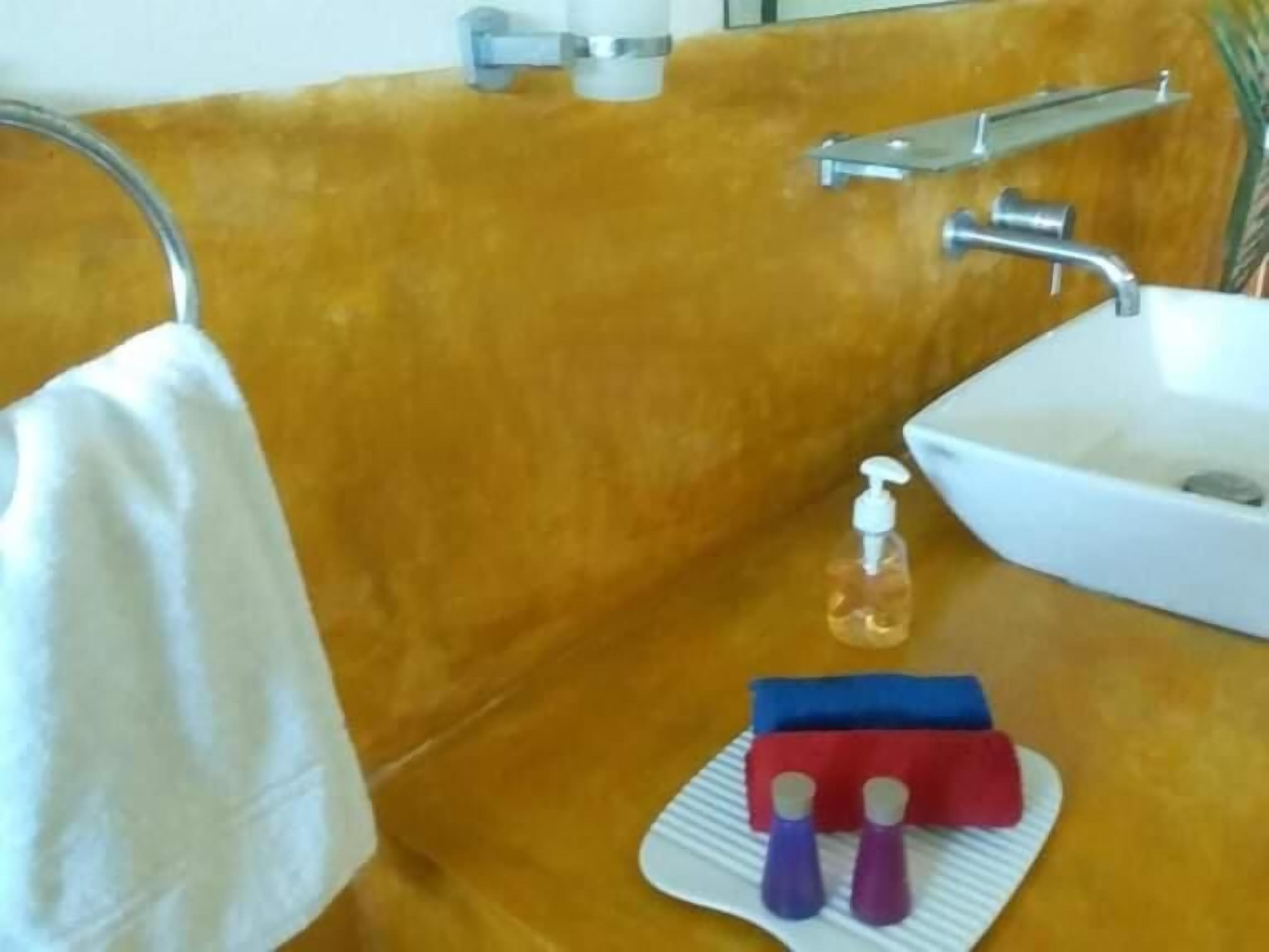 Een badkamer met een wit wastafelmeubel, een spiegel, een handdoek aan een rek en een zeepdispenser op het aanrecht.