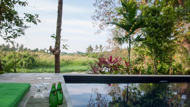 A poolside area with a table set for two, featuring a green mat, two wine glasses, and two green bottles.