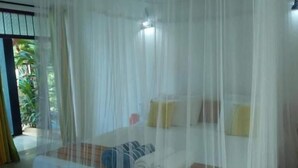 A room with a bed covered by a white canopy, a small table, and a chair.