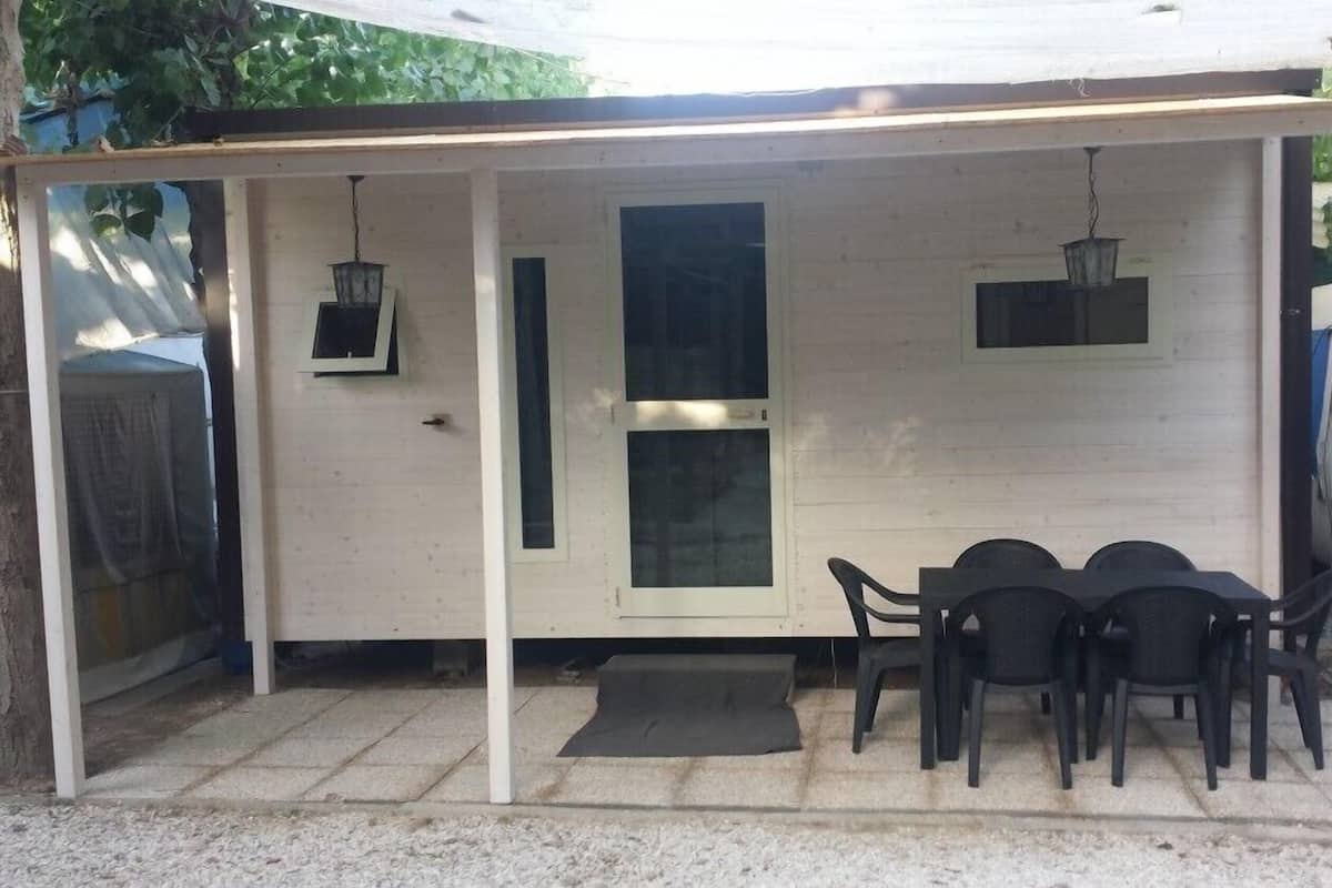 A covered outdoor seating area with a table and chairs, a door, and two hanging lanterns.