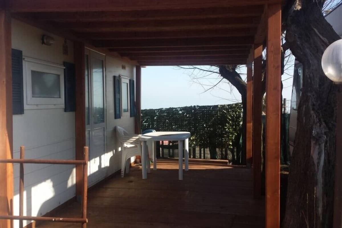 A covered outdoor area with a wooden floor, a white table, and a bench.