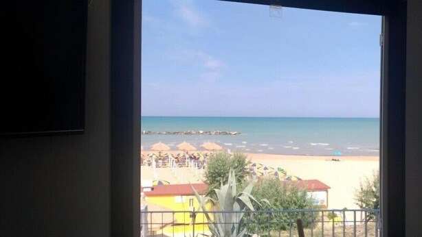 A view of a beach with umbrellas and a building in the foreground. - Camping Borghetti (Ortona)