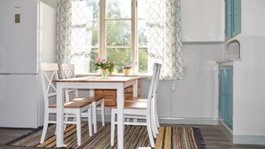 Una pequeña cocina con un refrigerador blanco, una mesa de madera con cuatro sillas y una ventana con cortinas estampadas.