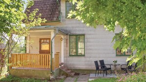 Una casa de dos pisos con un porche, un jardín pequeño y mobiliario exterior.
