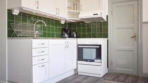 Cocina compacta con armarios blancos, horno empotrado, cafetera y salpicadero con azulejos verdes.