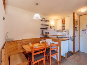 A compact kitchen with a wooden dining table and chairs, a built-in oven, and a hanging light fixture.