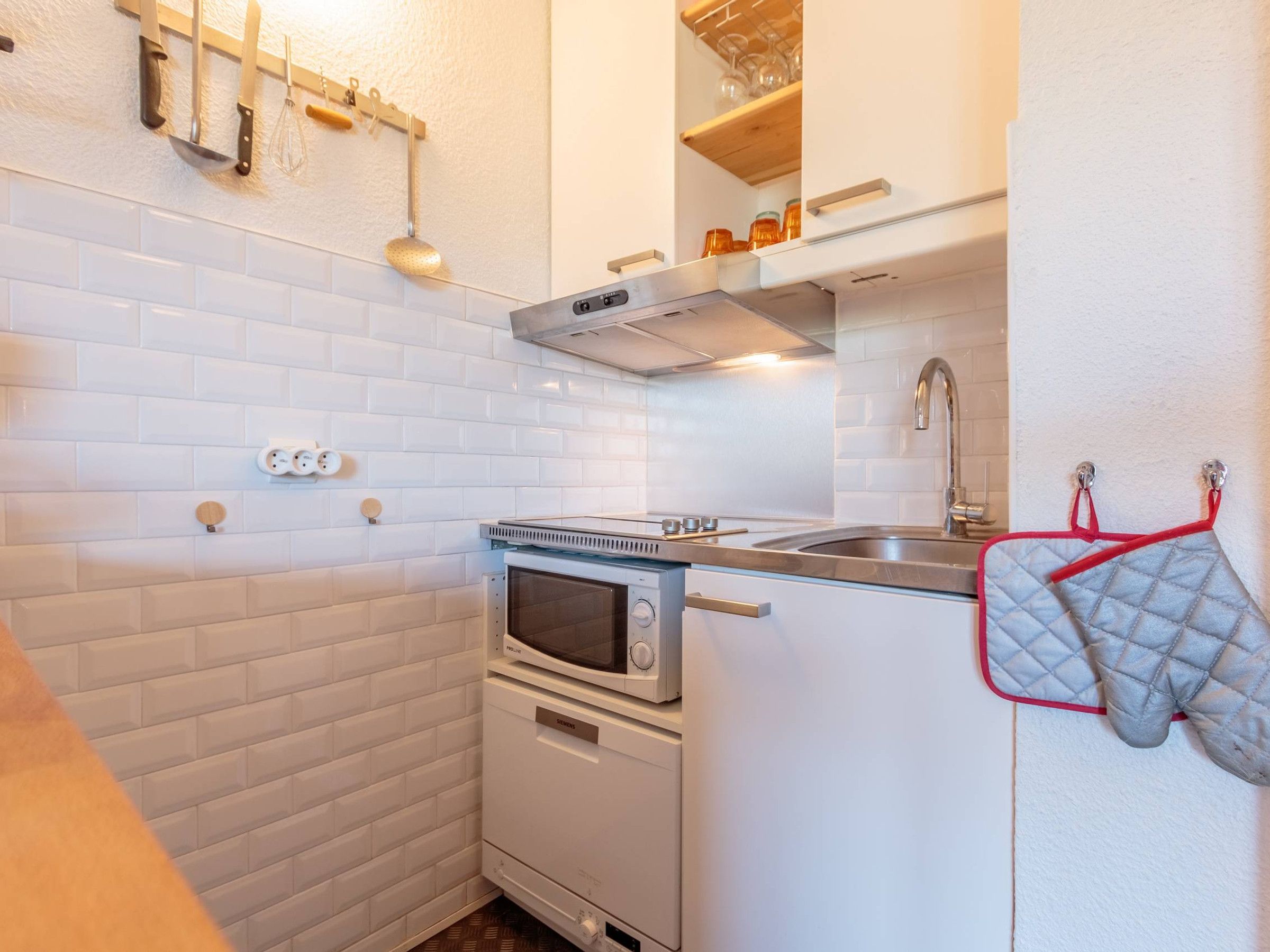 A compact kitchen with white subway tiles, a built-in oven, a microwave, and a stainless steel sink.