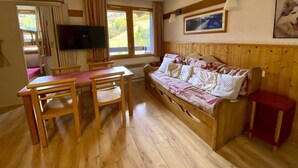 A cozy room with a wooden floor, a sofa, a dining table with chairs, a TV mounted on the wall, and a window with curtains. - 43m² Apartment in Plagne 1800, pets allowed, parking included (La Plagne 1800)