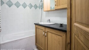 A bathroom with a bathtub, a sink, wooden cabinets, and a shower.