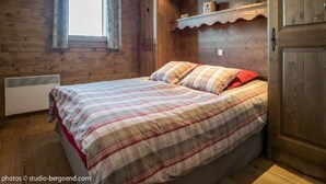 A wooden room with a bed, a window, and a shelf with decorative items.