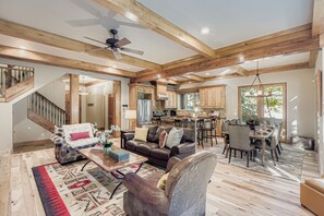 A spacious living area with a high ceiling, wooden beams, a fireplace, a dining area with a table and chairs, and a kitchen in the background. - Telemark Mountain Retreat Luxury 5BR Deer Valley Home 2665 (Park city)