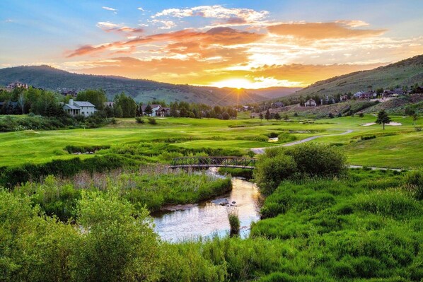 Stunning mountain valley with golf course, river, and residential homes under dramatic sunset sky.