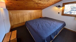 Ein kleiner, gemütlicher Raum mit schragem Dach, Holzwänden, einem Einzelbett, einer Bank und einem Fenster mit Blick.