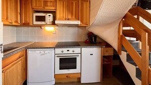 Eine kompakte Küche mit Holzschränken, einer Mikrowelle, einer Kaffeemaschine, einem Geschirrspüler und einem Herd.