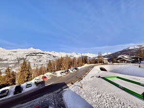 A snow-covered road with cars parked on the side, a ski lift, and mountains in the background. - Cozy duplex for 6 in La Plagne, ski-in/ski-out (La Plagne)