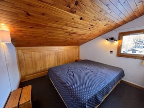 Une petite pièce agréable, avec un plafond en pente, des murs en bois, un lit simple, un banc et une fenêtre donnant sur un beau paysage.