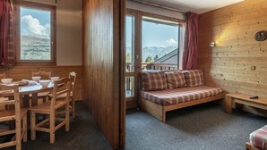 Ein gemütlicher Raum mit Holzvertäfelung, einem Esstisch mit Stühlen, einer Couch und Bergblick durch große Fenster.