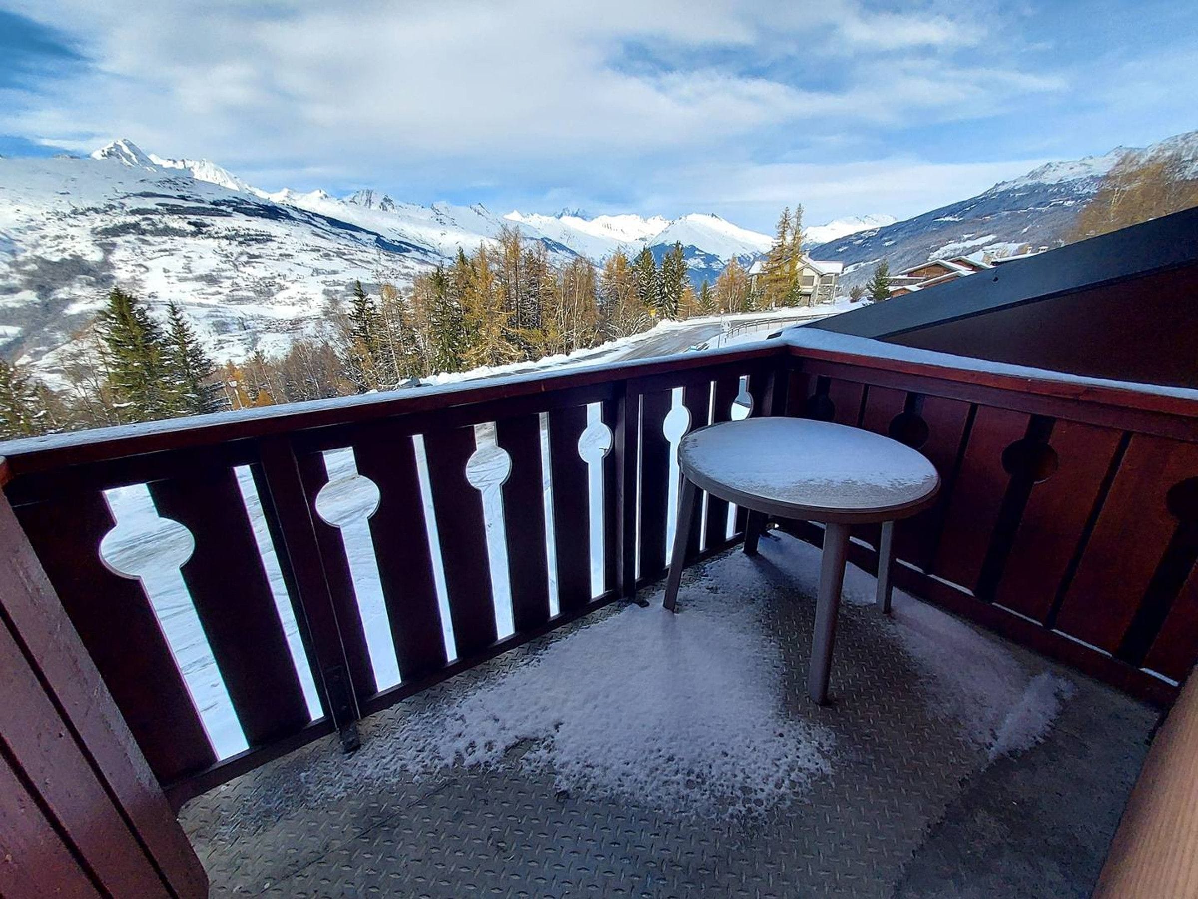 A balcony with a metal table and chairs, overlooking a snowy mountain landscape.