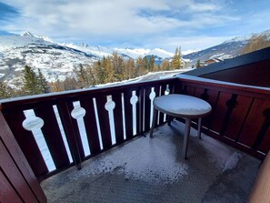 Un balcón con una mesa y sillas de metal, con vistas a un paisaje montañoso nevado.