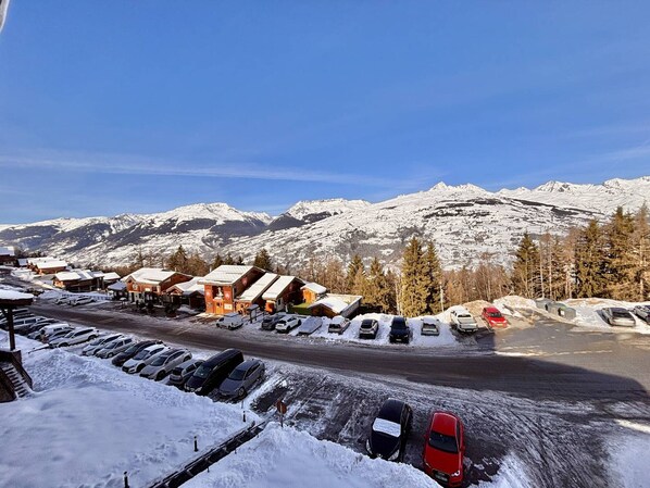 A snow-covered parking lot with several cars and a building with a red roof in the foreground.