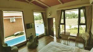 A room with a bed, a fan, wicker chairs, and large windows with curtains. - Sixth Element (Somvarpet)