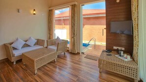 A room with a wicker sofa set, a small table, a TV mounted on the wall, and a view of the outside. - Sixth Element (Somvarpet)