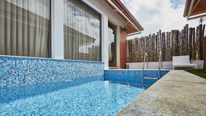 A swimming pool with blue mosaic tiles, a wooden fence, and a white outdoor seating area. - Sixth Element (Somvarpet)