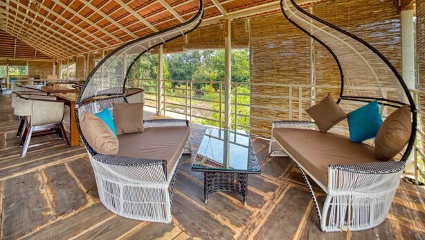 A covered outdoor seating area with wicker furniture and a glass table. - Sixth Element (Somvarpet)
