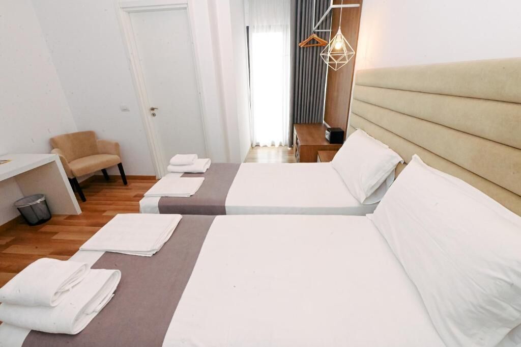 A hotel room with two beds, a chair, a desk, and a hanging light fixture.