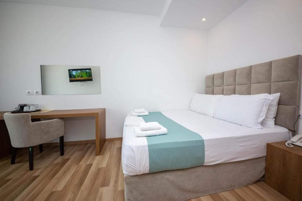 Una camera d'hotel con un letto, una scrivania, una sedia, una TV montata a parete e un telefono sul comodino.