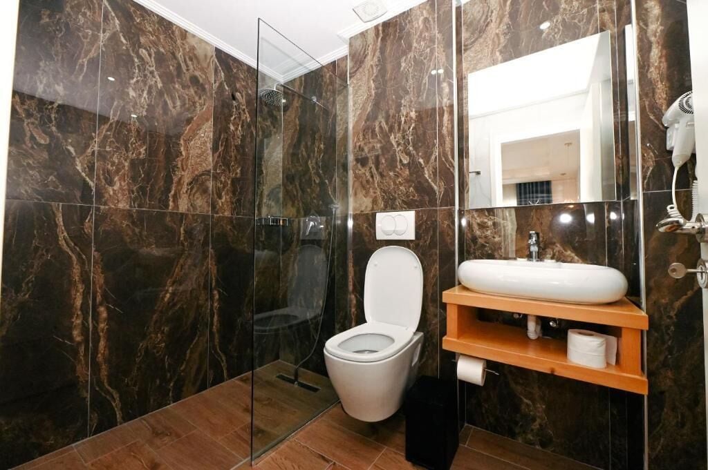 A modern bathroom with a glass-enclosed shower, a white toilet, and a marble-tiled wall.