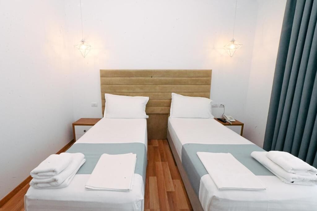 A double room with two beds, each with a wooden headboard, white bedding, and a nightstand with a lamp.