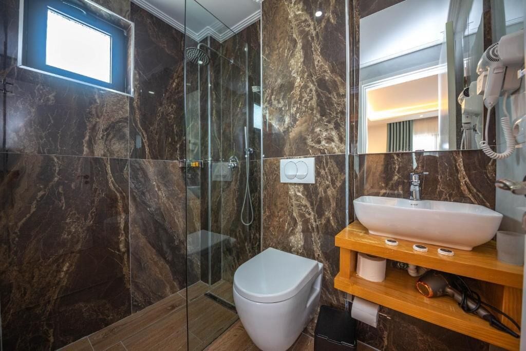 Ein modernes Badezimmer mit einer gläsernen Duschkabine, einer weißen Toilette und einer Marmor-Spritzschutzwand.