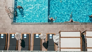 A swimming pool with people swimming and sunbathing. There are lounge chairs and umbrellas. - Bianco Hotel (Ksamil)