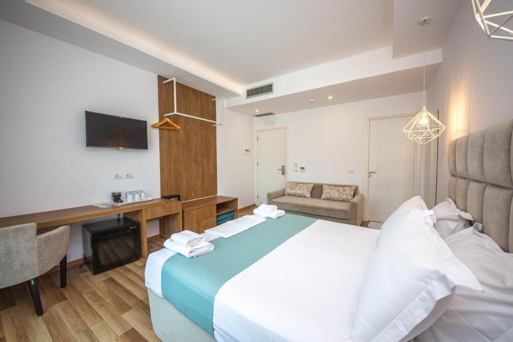 A modern hotel room with a bed, a desk, a chair, a TV, and a wardrobe.