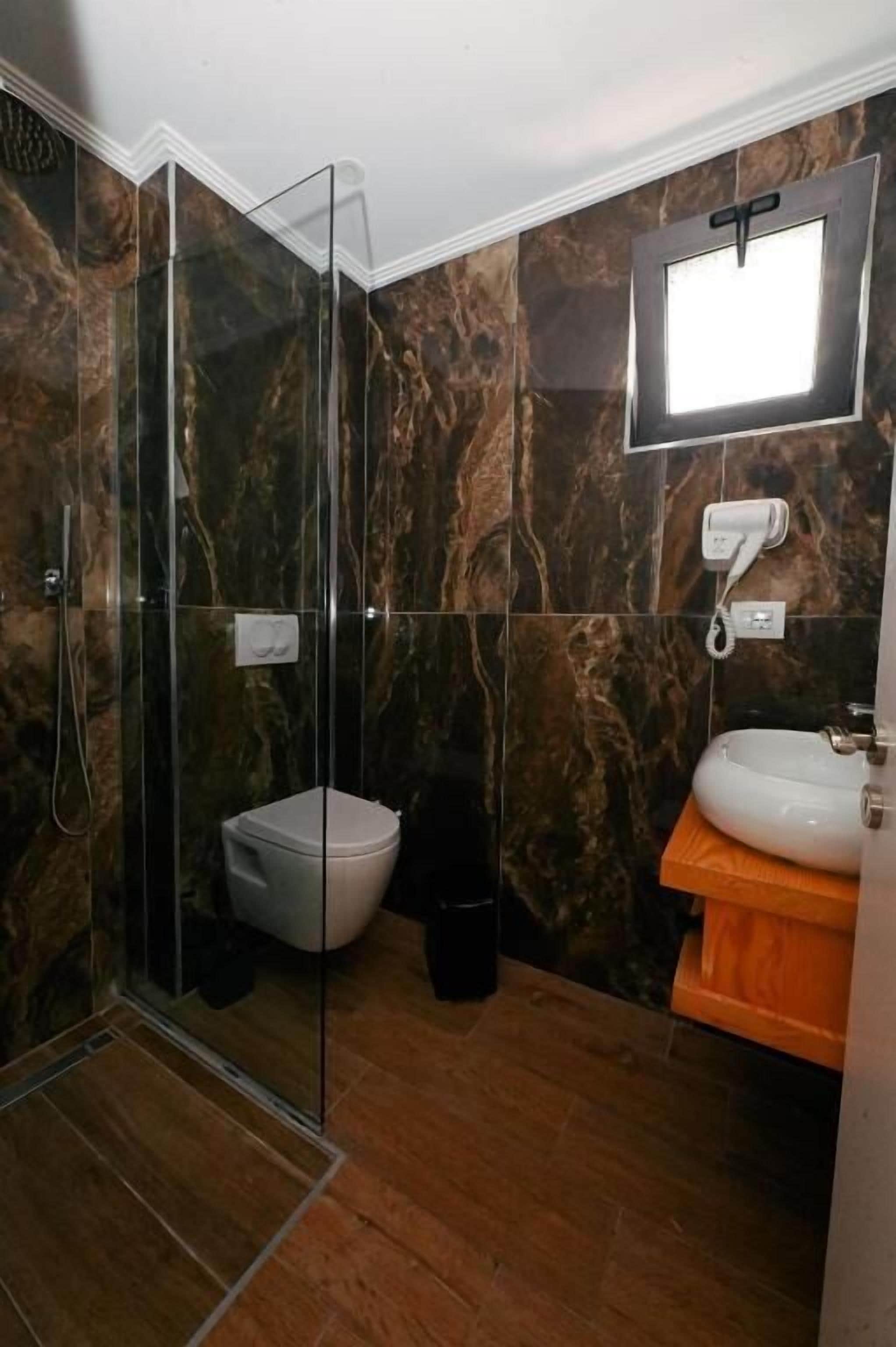 A bathroom with a glass-enclosed shower, a toilet, and a sink with a mirror above it.