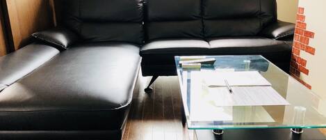 Ein schwarzes Ledersofa mit einem Glastisch in einem Raum mit Holzboden.