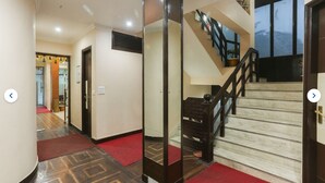 Un pasillo de hotel con alfombra roja, una escalera con barandillas negras y vistas al exterior a través de una ventana.