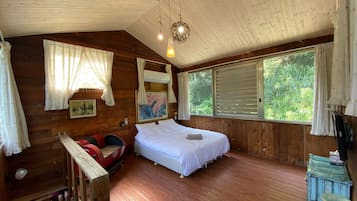 Ein Schlafzimmer einer Holzhütte mit einem Bett, einem kleinen Tisch und einem Fenster mit Jalousien.