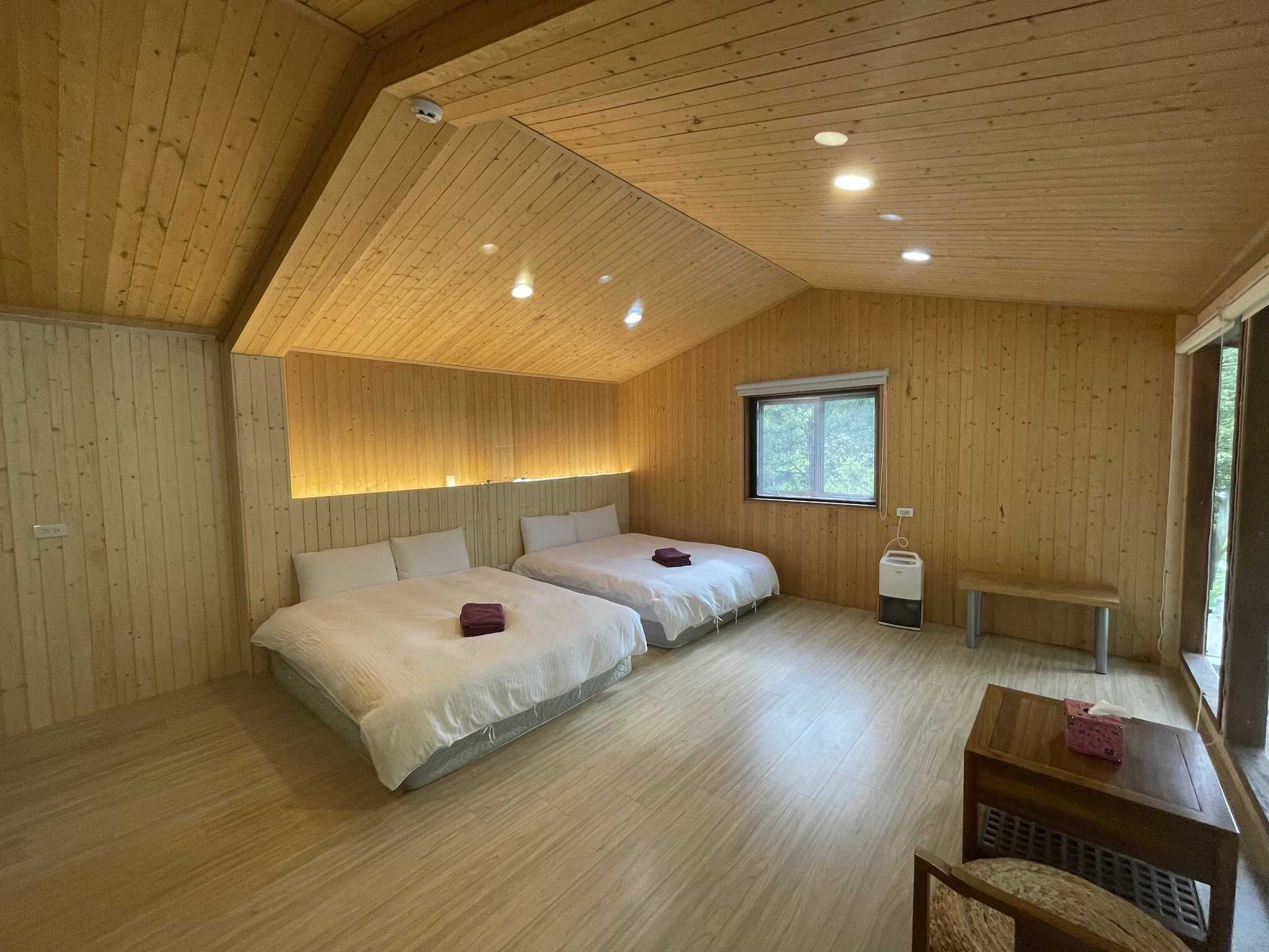 A room with two beds, wooden walls, a window, and a small table with a tissue box.