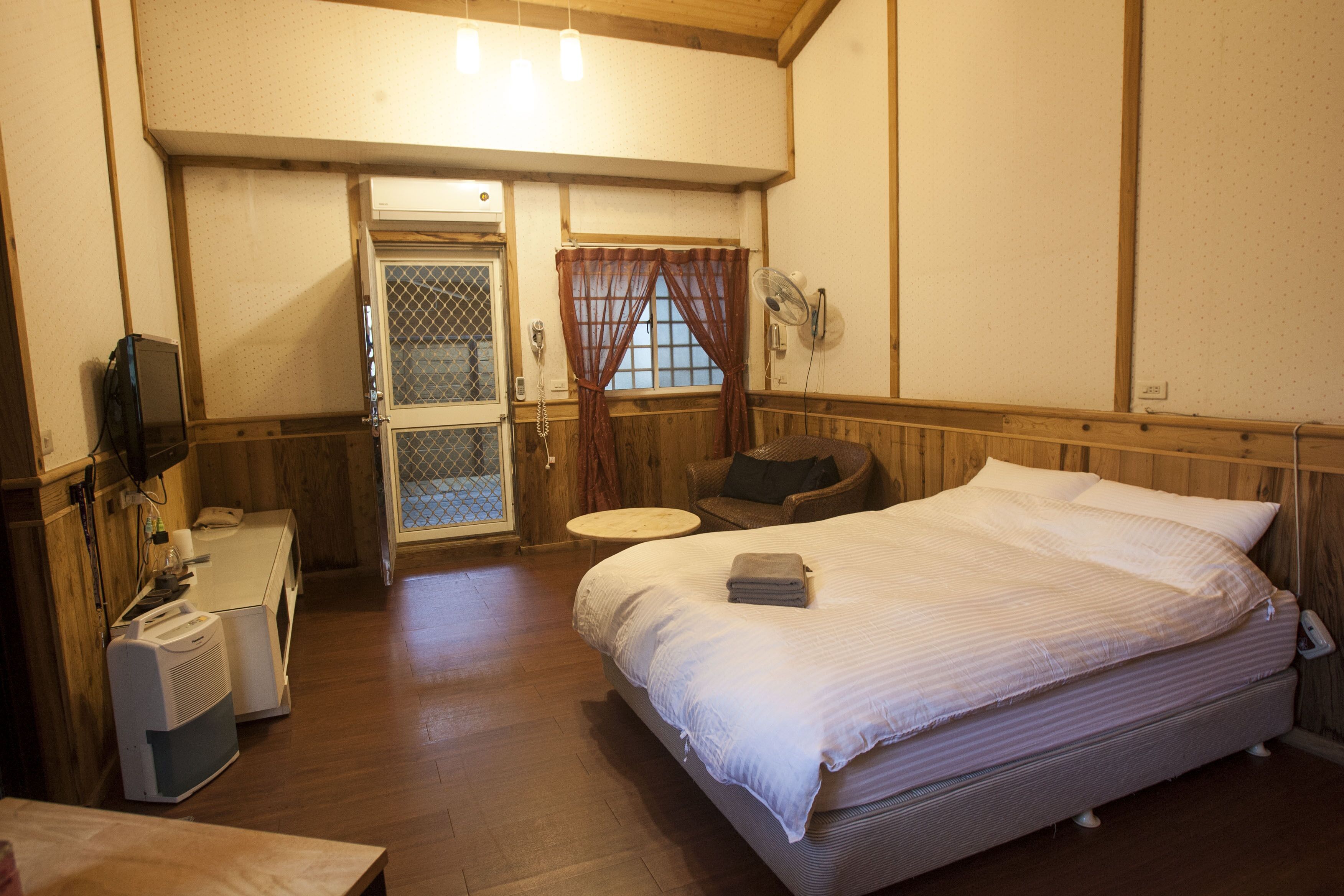Habitación de hotel con cama, escritorio con teléfono, silla, una mesita y ventana con cortinas.