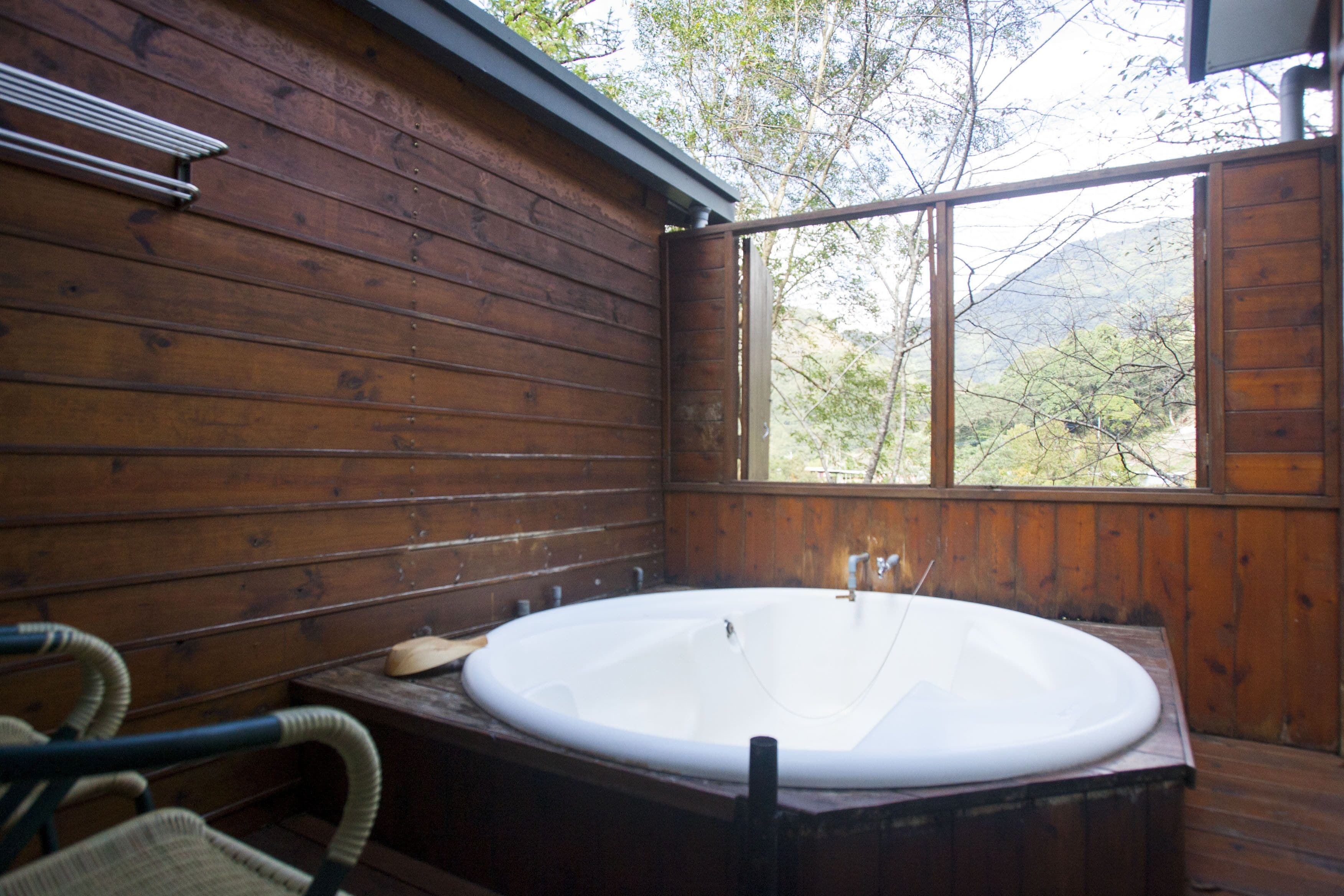 A wooden cabin with a large bathtub, wooden walls, and a window overlooking a mountainous area.