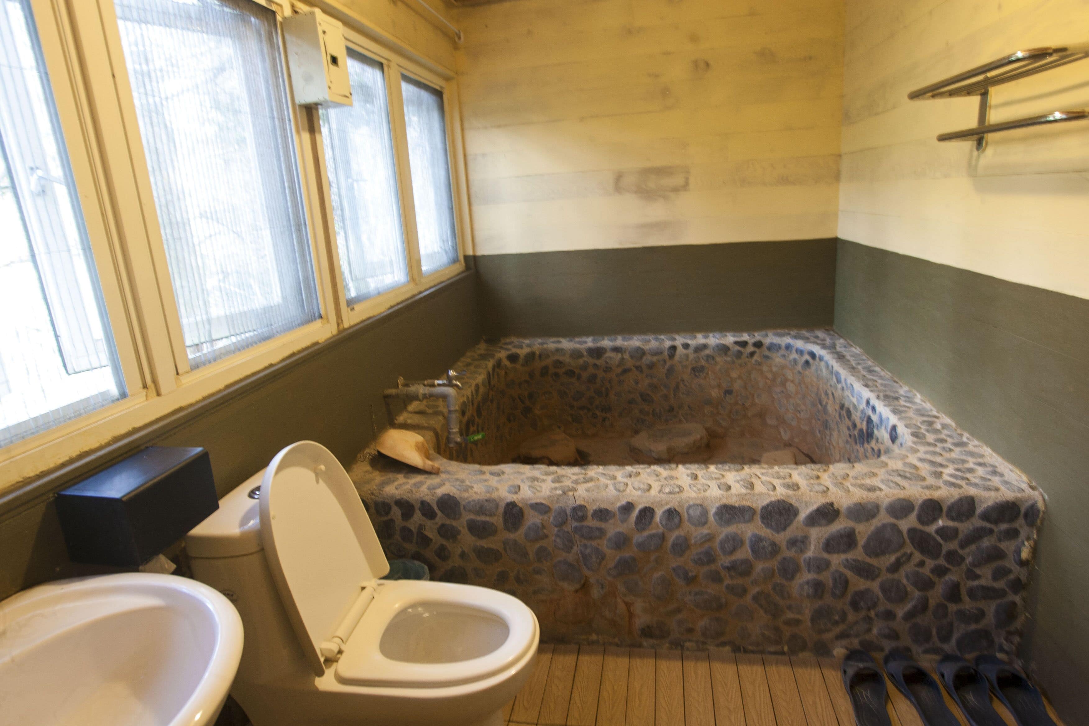 A bathroom with a stone bathtub, a toilet, and a sink.