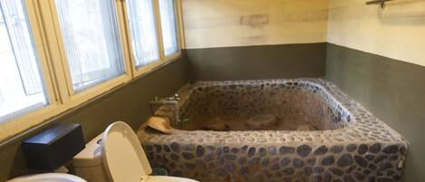 A bathroom with a stone bathtub, a toilet, and a sink.