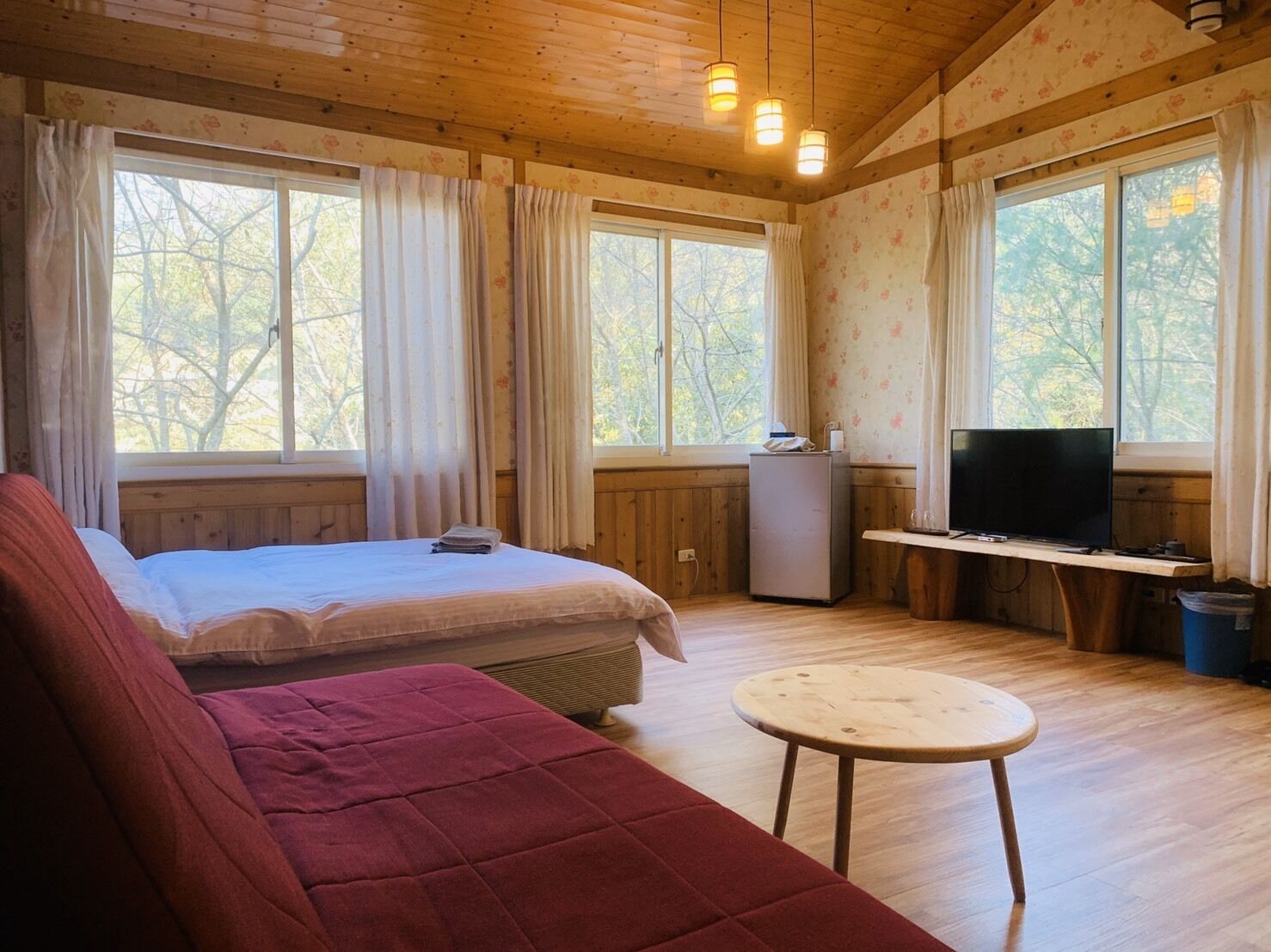 Ein gemütliches Zimmer mit einem Bett, einem roten Sofa, einem kleinen Tisch, einem Fernseher und einem Fenster mit Vorhängen.